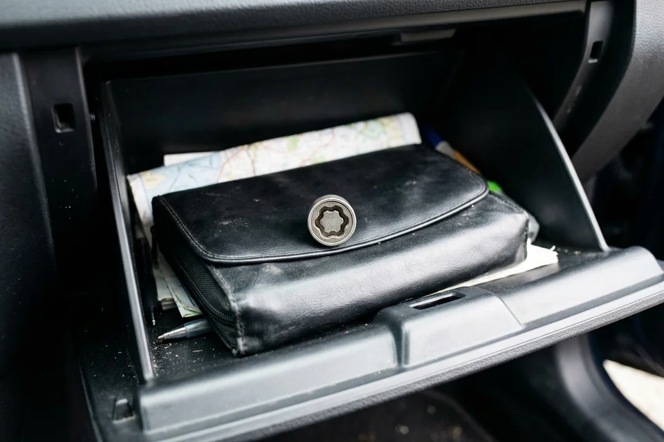Open glove box with the owner's manual pouch and a small patterned lock key socket resting on top
