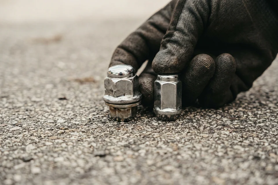 Two-piece lug nut with a swollen chrome cap held next to an undamaged one, the size difference visible
